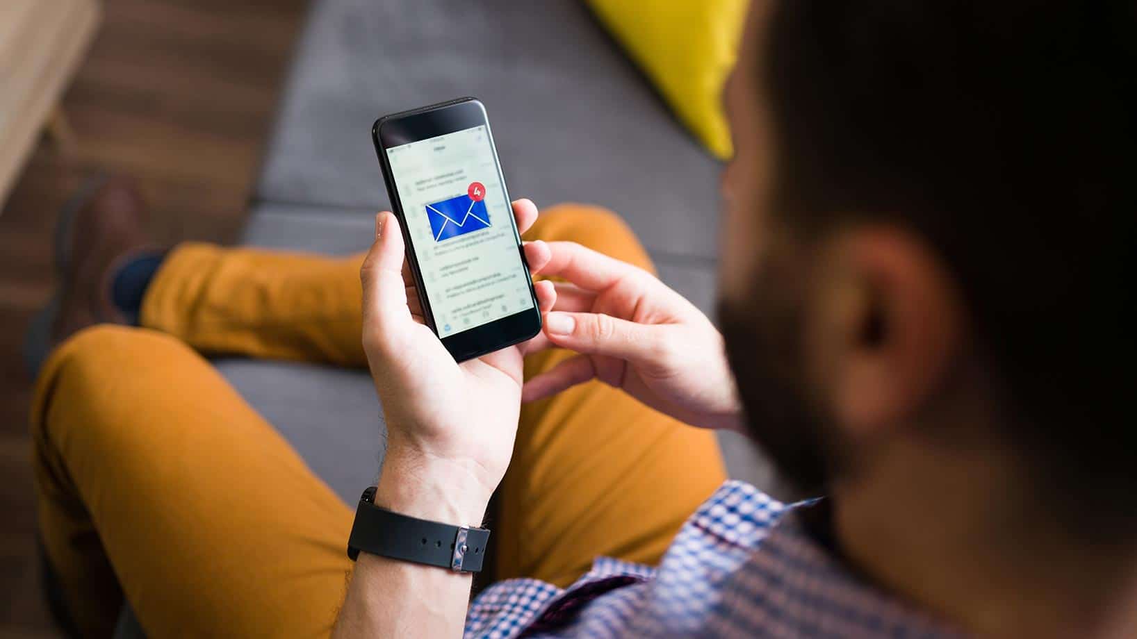 Das Bild zeigt einen Mann mit einem Smartphone in der Hand, auf dem ein E-Mail-Postfach geöffnet ist und neue Nachrichten vorhanden sind.